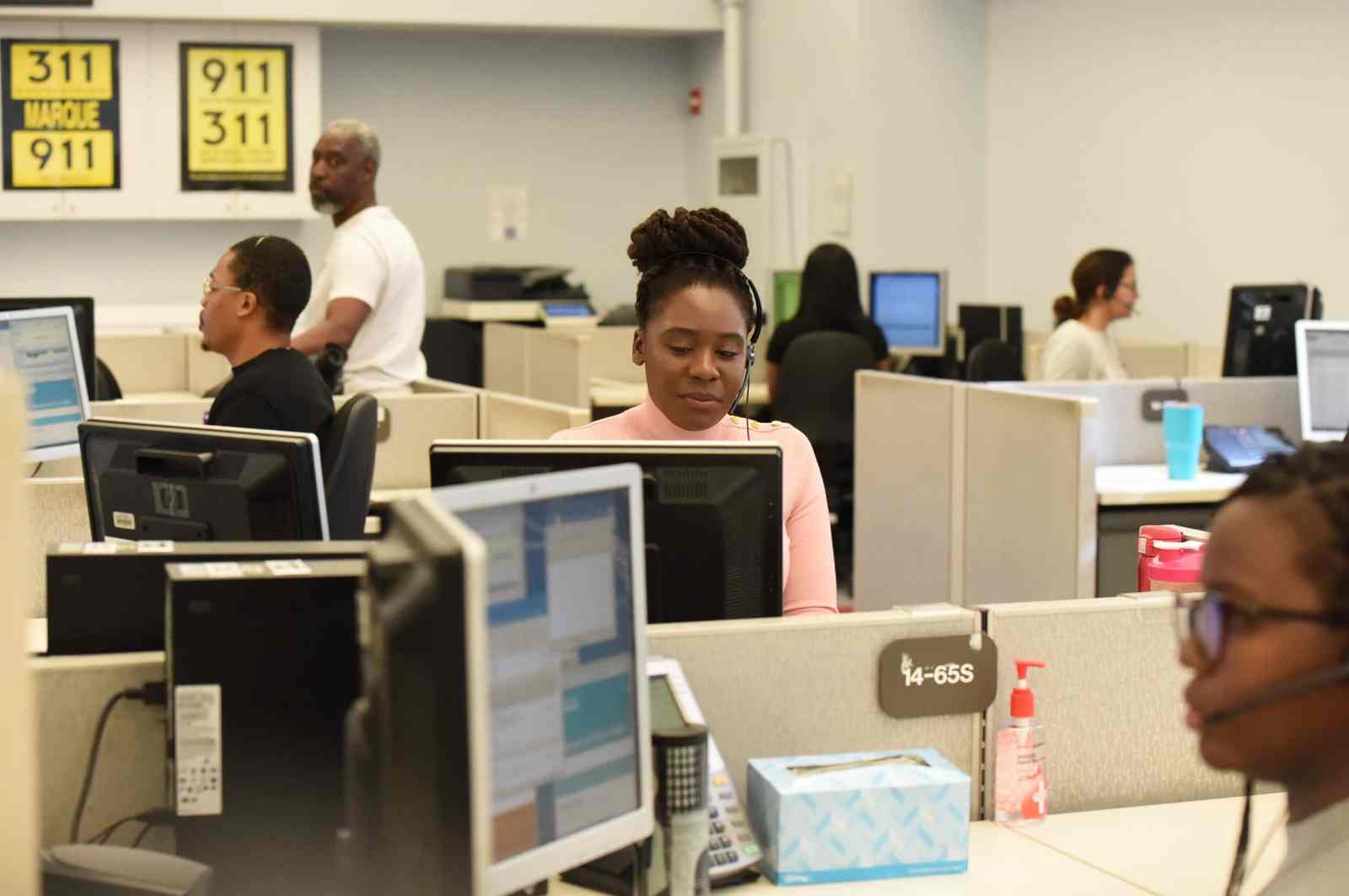 people working in a office setting, a woman with a head set is featured in the middle of the scene